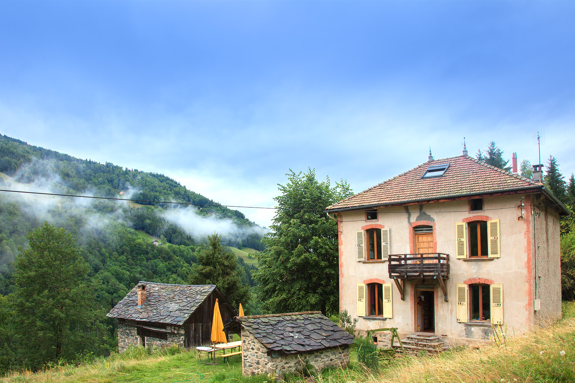 Maison de famille en bois et pierre dans une clairière de montagne